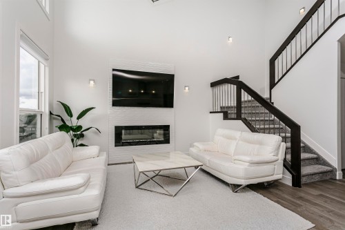 Two-story living area featuring a modern fireplace with textured tile surround, wood-finish flooring, and a contemporary staircase with dark wood railings and metal spindles - 9107 181 Avenue Nw, Edmonton, AB 