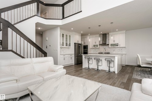 Two-story ceiling, contemporary staircase with dark wood-finish railing, wood-finish flooring, white cabinetry with integrated appliances, kitchen island with seating - 9107 181 Avenue Nw, Edmonton, AB 