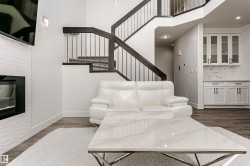 Contemporary fireplace with a textured surround, wood-finish flooring, built-in cabinetry with glass-front uppers, and an open staircase with dark wood handrails and metal balusters - 