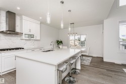 Modern kitchen featuring a large island with seating, stainless steel appliances, white cabinetry, and wood-finish flooring - 