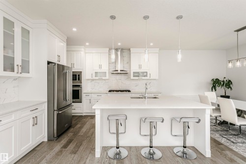 White cabinetry, stainless steel appliances, large kitchen island, wood-finish flooring, and pendant lighting - 9107 181 Avenue Nw, Edmonton, AB 