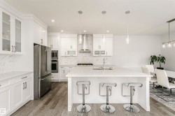 White cabinetry, stainless steel appliances, large kitchen island, wood-finish flooring, and pendant lighting - 