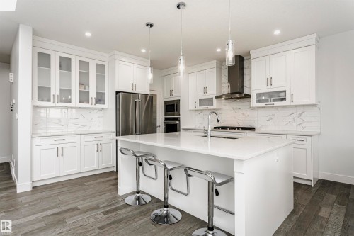 Contemporary white cabinetry with glass-front accents, white countertop island, stainless steel appliances, and wood-finish flooring - 9107 181 Avenue Nw, Edmonton, AB 