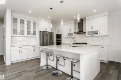 Contemporary white cabinetry with glass-front accents, white countertop island, stainless steel appliances, and wood-finish flooring - 