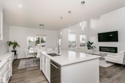 Open-concept living area with wood-finish flooring, white cabinetry, a kitchen island with an undermount sink, a sleek linear fireplace, and high ceilings - 