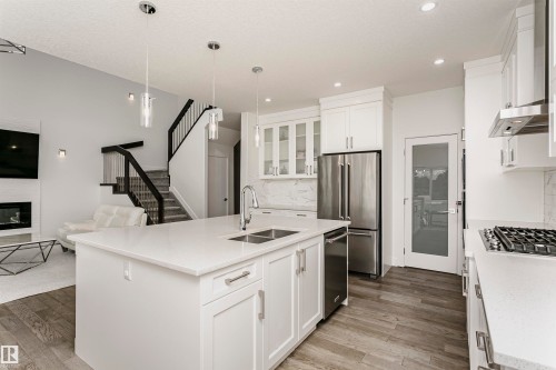 Open-concept kitchen featuring an island with a double sink, stainless steel appliances, white cabinetry, and wood-finish flooring - 9107 181 Avenue Nw, Edmonton, AB 