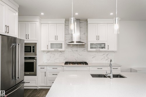 White shaker-style cabinetry, stainless steel appliances, marble-look backsplash, quartz countertops, and pendant lighting - 9107 181 Avenue Nw, Edmonton, AB 