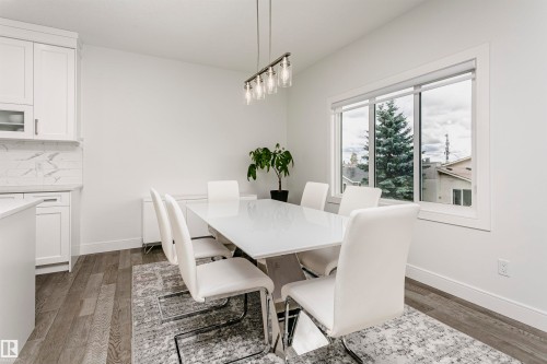 White kitchen cabinetry with glass-front accents, marble-look backsplash, light wood-finish flooring, and a large window - 9107 181 Avenue Nw, Edmonton, AB 