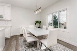 White kitchen cabinetry with glass-front accents, marble-look backsplash, light wood-finish flooring, and a large window - 