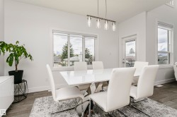 Open-concept dining area featuring wood-finish flooring, a modern chandelier with clear glass shades, large windows with white trim, and a glass-paneled exterior door - 