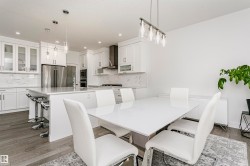 Modern kitchen and dining area featuring recessed lighting, stainless steel appliances, white cabinetry, a kitchen island with seating, and wood-finish flooring - 