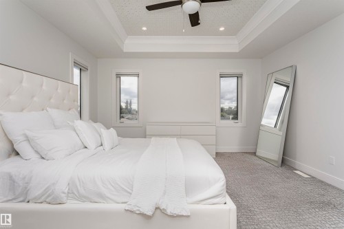 Tray ceiling with recessed lighting and ceiling fan, two windows, textured carpeting, and white walls - 9107 181 Avenue Nw, Edmonton, AB 