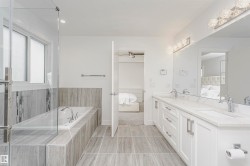 Dual vanity with stone countertops and undermount sinks, glass-enclosed shower, soaking tub, and tile flooring - 