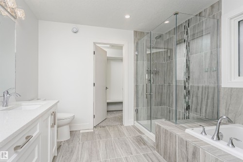 Dual vanity with chrome fixtures and undermount sinks, walk-in shower with glass enclosure and tiled walls, built-in bathtub with tiled surround, and gray wood-finish tile flooring - 9107 181 Avenue Nw, Edmonton, AB 