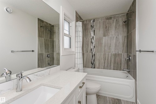 White vanity with a quartz countertop and integrated sink, polished chrome faucet, and full-width mirror - 9107 181 Avenue Nw, Edmonton, AB 