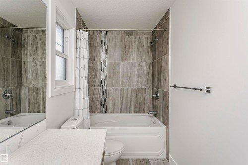 Bathtub with integrated shower, wood-finish tile surround, and mosaic accent - 9107 181 Avenue Nw, Edmonton, AB 