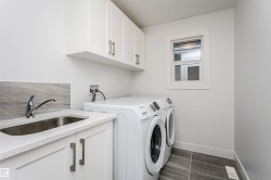 Laundry area featuring upper cabinetry, a utility sink with a stone backsplash, a window, and tiled flooring - 