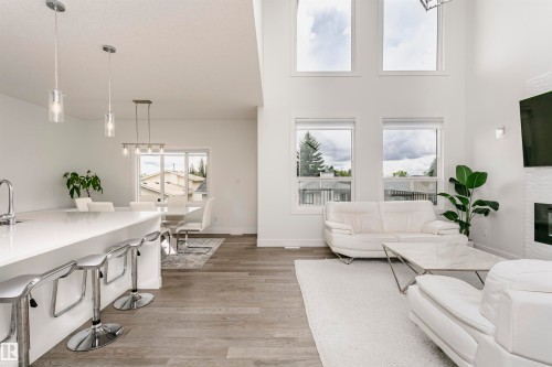 Open-concept living area with soaring ceilings, wood-finish flooring, a contemporary fireplace, and an expansive kitchen island with a white countertop - 9107 181 Avenue Nw, Edmonton, AB 