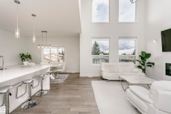 Open-concept living area with soaring ceilings, wood-finish flooring, a contemporary fireplace, and an expansive kitchen island with a white countertop - 