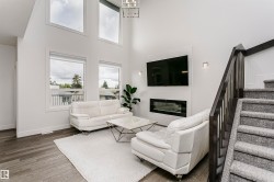 Living area featuring a modern linear fireplace with a textured tile surround, high ceilings, large windows, wood-finish flooring, and a dark wood staircase with carpeted treads - 