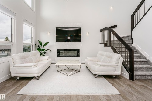 Two-story living area with wood-finish flooring, a contemporary fireplace feature, and a dark wood staircase with metal balusters - 9107 181 Avenue Nw, Edmonton, AB 
