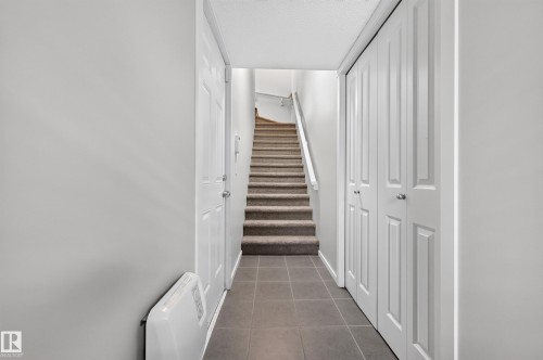 Hallway from garage to second floor featuring tiled flooring, carpeted staircase, paneled interior doors, and bi-fold closet doors - #72 603 Watt Bv Sw Sw, Edmonton, AB 