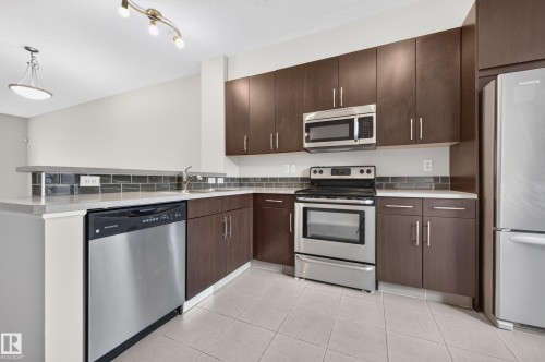 Stainless steel appliances, wood-finish cabinetry, light-toned countertops, subway tile backsplash, and light-colored tile flooring - #72 603 Watt Bv Sw Sw, Edmonton, AB 
