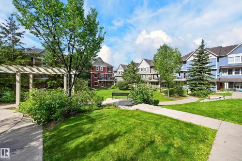 Manicured communal green spaces with mature trees, paved walkways, and an architectural pergola - #72 603 Watt Bv Sw Sw, Edmonton, AB 