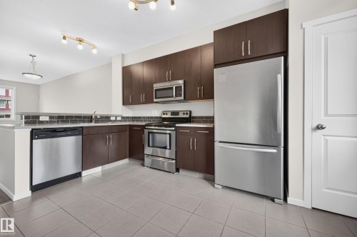 Kitchen featuring wood-finish cabinetry, stainless steel appliances, a subway tile backsplash, and light gray floor tiling - #72 603 Watt Bv Sw Sw, Edmonton, AB 