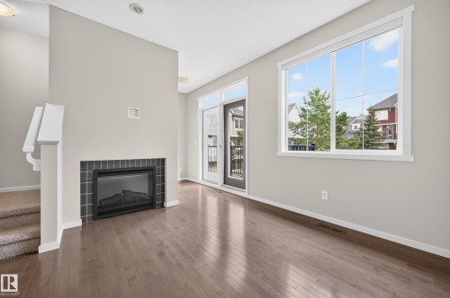 Wood-finish flooring, built-in fireplace with dark tile surround, white trim, sliding glass door with balcony, and large window - #72 603 Watt Bv Sw Sw, Edmonton, AB 