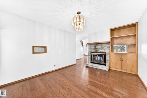 Hardwood flooring, stone-clad fireplace with hearth, built-in shelving, built-in cabinetry, and a modern ceiling fixture - 4208 Ramsay Road Nw, Edmonton, AB 