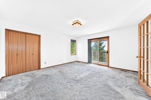 Sliding glass door leading to a balcony, wood-finish bi-fold closet doors, transom glass panel door, flush mount ceiling light fixture, and a window with wood trim - 4208 Ramsay Road Nw, Edmonton, AB 
