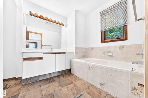 Tile flooring, white vanity with integrated sink, large wall-mounted mirror, vanity lighting fixture, tiled bath surround - 4208 Ramsay Road Nw, Edmonton, AB 