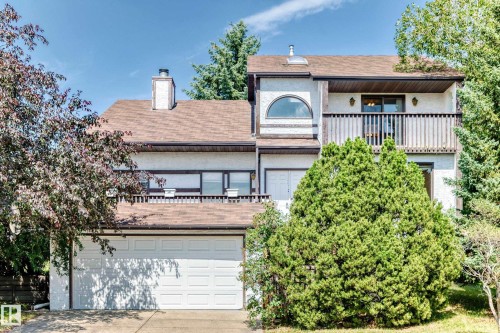 Two-story residence with a two-car garage, a second-story balcony with wood railing, an arched window, and a prominent chimney - 4208 Ramsay Road Nw, Edmonton, AB 