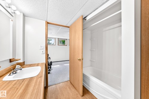 White drop-in bathtub with integrated shelving, wood-finish flooring, and a wood-finish vanity with an integrated sink - 4208 Ramsay Road Nw, Edmonton, AB 