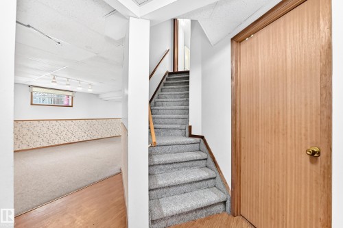 Carpeted staircase with wood-finish handrail, leading to a finished lower level with carpeted flooring and a drop ceiling - 4208 Ramsay Road Nw, Edmonton, AB 