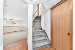 Carpeted staircase with wood-finish handrail, leading to a finished lower level with carpeted flooring and a drop ceiling - 