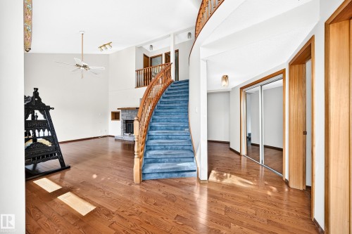 Curved staircase with wood railing, wood-finish flooring, stone fireplace, vaulted ceiling, and sliding mirrored closet doors - 4208 Ramsay Road Nw, Edmonton, AB 
