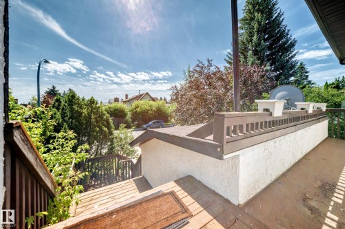 Outdoor deck with wood railings, a white textured wall, and mature surrounding foliage - 4208 Ramsay Road Nw, Edmonton, AB 