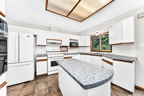 Kitchen featuring white cabinetry, a center island with a curved countertop, tile flooring, and integrated white appliances - 4208 Ramsay Road Nw, Edmonton, AB 