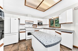 Kitchen featuring white cabinetry, a center island with a curved countertop, tile flooring, and integrated white appliances - 