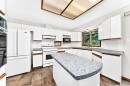 Kitchen featuring white cabinetry, a center island with a curved countertop, tile flooring, and integrated white appliances - 4208 Ramsay Road Nw, Edmonton, AB 