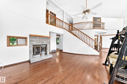 Hardwood flooring, two-story living area, stone-surround fireplace, ceiling fan, and curved staircase with wood banister - 4208 Ramsay Road Nw, Edmonton, AB 