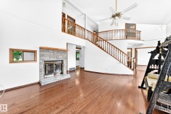 Hardwood flooring, two-story living area, stone-surround fireplace, ceiling fan, and curved staircase with wood banister - 