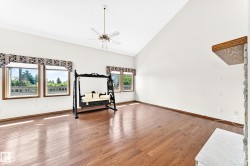 Vaulted ceiling, wood-finish flooring, multiple windows, built-in stone fireplace with wood mantel, and ceiling fan - 