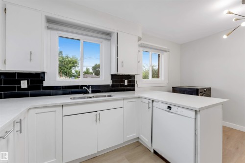 White cabinetry with brushed nickel hardware, a stainless steel double-basin sink, and a black subway tile backsplash - 7928 82 Avenue Nw, Edmonton, AB 
