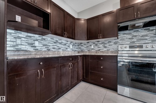 Dark wood-finish cabinetry, mosaic tile backsplash, solid surface countertops, and stainless steel oven with cooktop - 11421 82 Street Nw, Edmonton, AB 