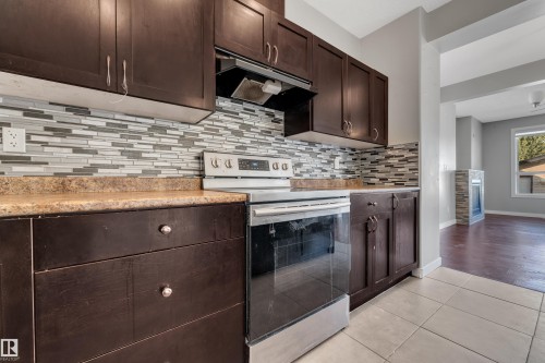 Dark wood-finish cabinetry with silver-tone hardware, a light-toned countertop, and a mosaic tile backsplash - 11421 82 Street Nw, Edmonton, AB 