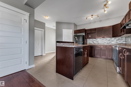 Kitchen featuring dark wood-finish cabinetry, a central island with an integrated sink, patterned tile backsplash, and light tile flooring - 11421 82 Street Nw, Edmonton, AB 