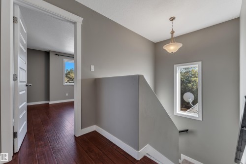 Hallway featuring wood-finish flooring, a white paneled door, and a decorative pendant light fixture - 11421 82 Street Nw, Edmonton, AB 